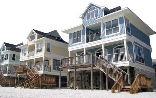 A row of houses on the beach with stairs going up them.